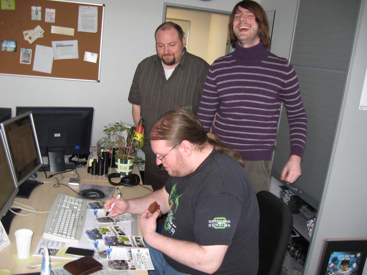 [17/11/2009] Autogramme gibt es auch anderswo. International Community Manager Sören Stöß und Oliver Tunkel von der Datenbank zeigen sich schwer beeindruckt von Michael Winters Multi-Tasking-Fähigkeiten. Kuchen essen, über Eintracht Frankfurt philosophieren und Autogramme schreiben gleichzeitig? Das kann nur 3D-Spiel-Guru „MiWi“.
