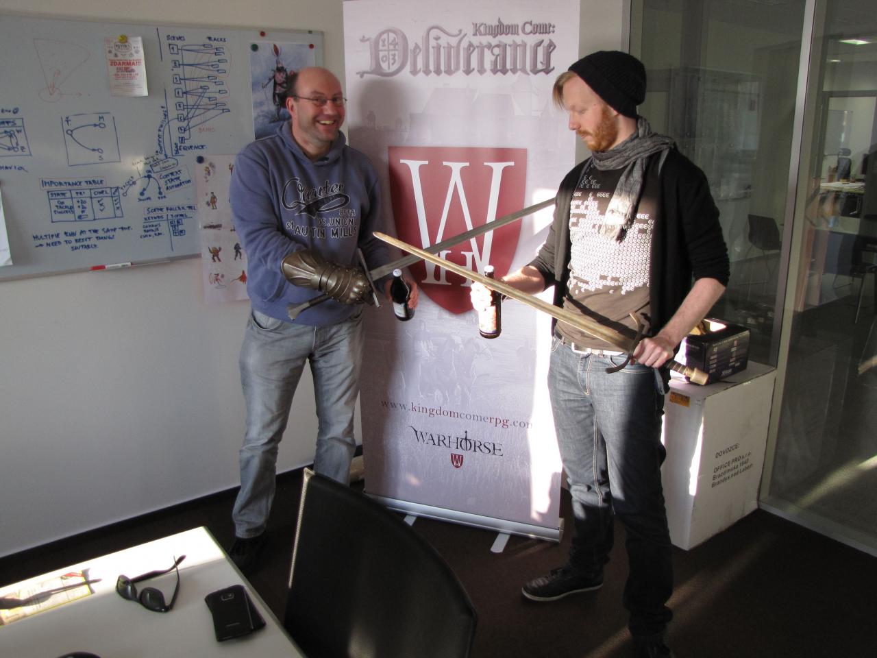 [13/04/2015] PC Games-Redakteur Stefan Weiß (links) zu Besuch bei den Prager Warhorse Studios. Community-Manager Tobias Stolz-Zwilling (rechts) zeigt Stefan, wie man zünftig die Klingen kreuzt und freut sich über das mitgebrachte fränkische Gastgeschenk in Form eines echten Ritterbiers.