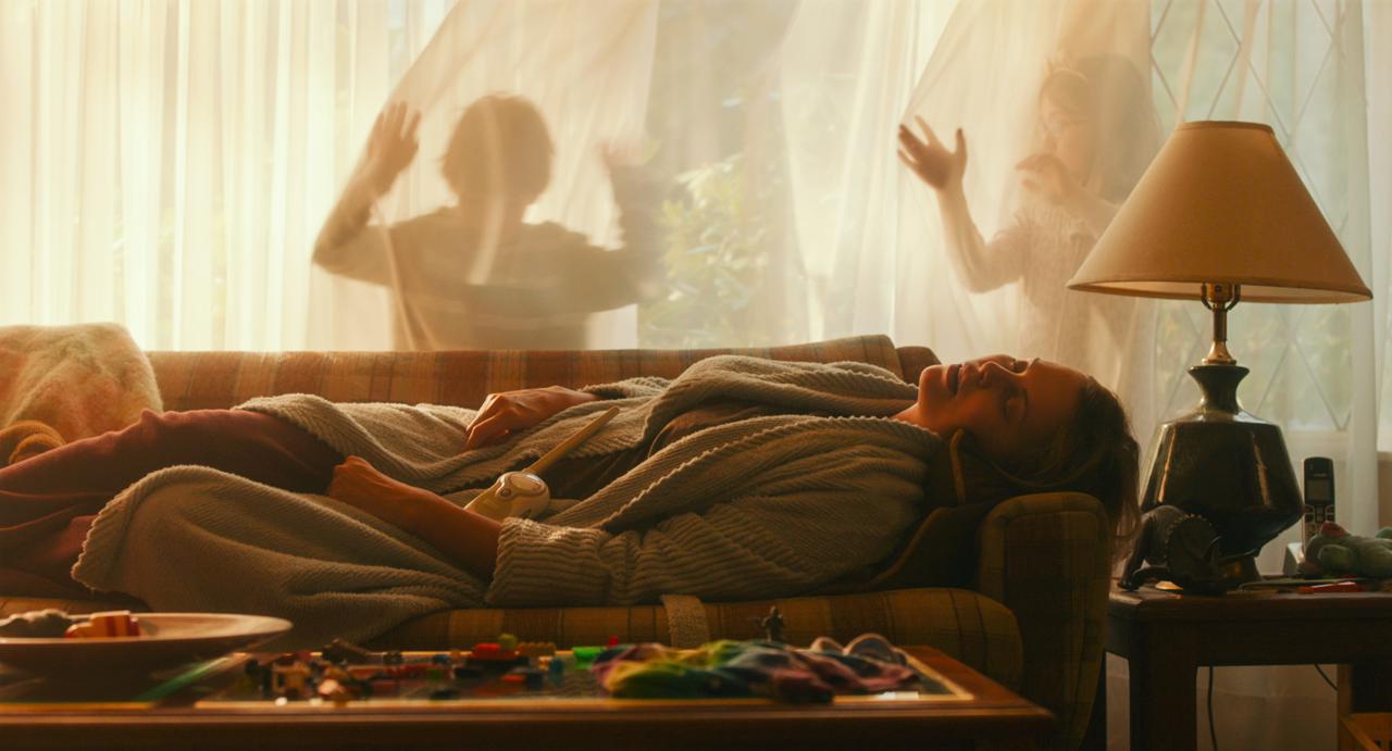 Szenenbild aus "Tully - Das verdammte Mutterglück" (2018) - Marlo schläft entkräftet auf der Couch, während ihre Kinder herumtollen.