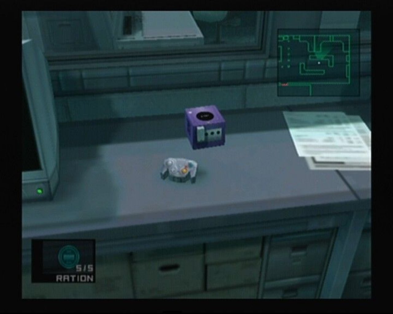 Ein Gamecube, der im Spiel Metal Gear Solid: The Twin Snakes auf einem Schreibtisch steht.