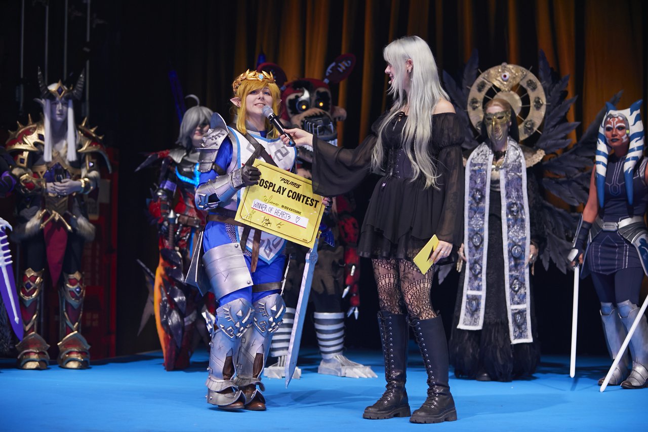 Die Gewinner der Herzen des Cosplay-Wettbewerbs steht gemeinsam mit einer Moderatorin auf der Bühne
