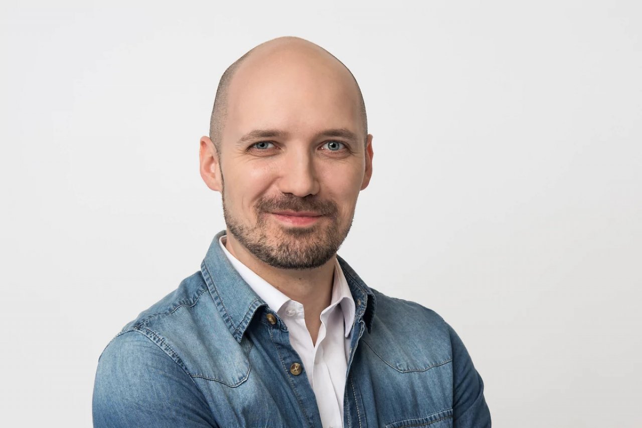 Weißer Mann in seinen Dreißigern mit Glatz, der direkt in die Kamera schaut