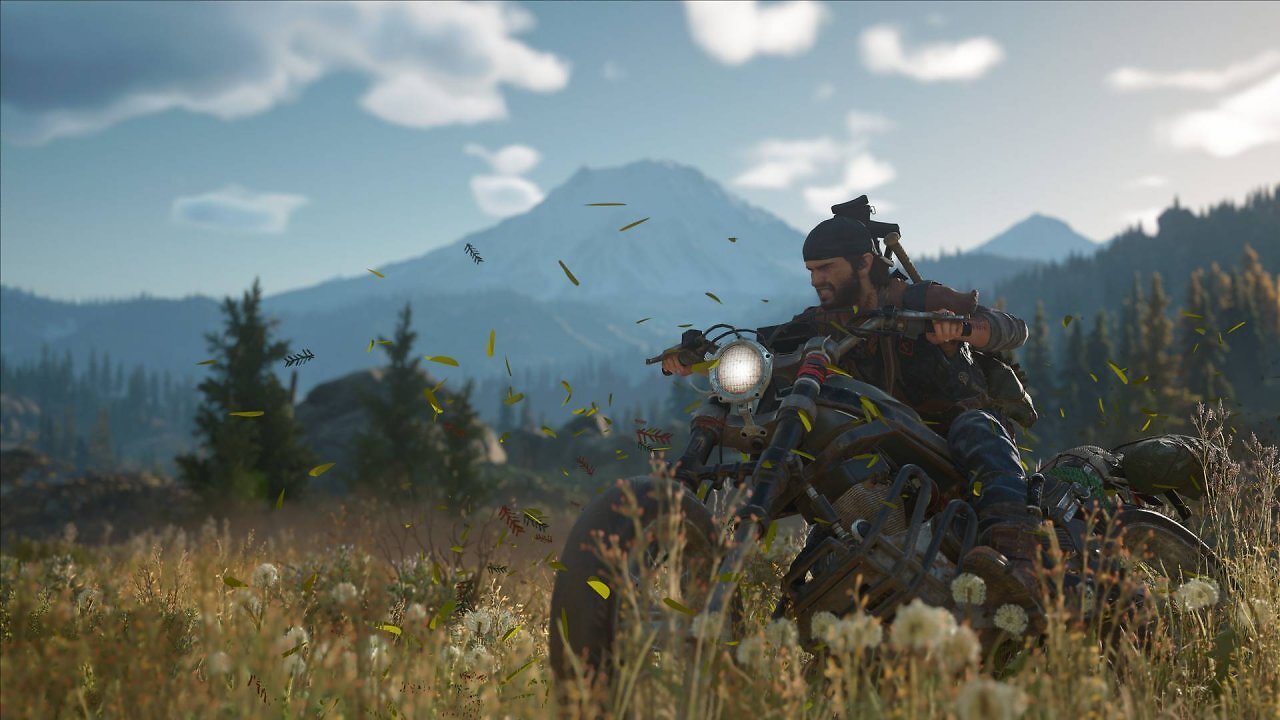 [08/09/2025] Protagonist Deacon St. John fährt auf seinem Motorrad durch eine bewaldete Landschaft in Days Gone, mit Bergen im Hintergrund und umherfliegenden Blättern.
