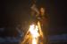 Nico Okano (Lyrica Okano) steht am Lagerfeuer in der finsteren Nacht.