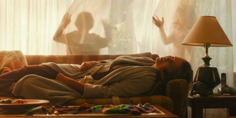 Szenenbild aus "Tully - Das verdammte Mutterglück" (2018) - Marlo schläft entkräftet auf der Couch, während ihre Kinder herumtollen.